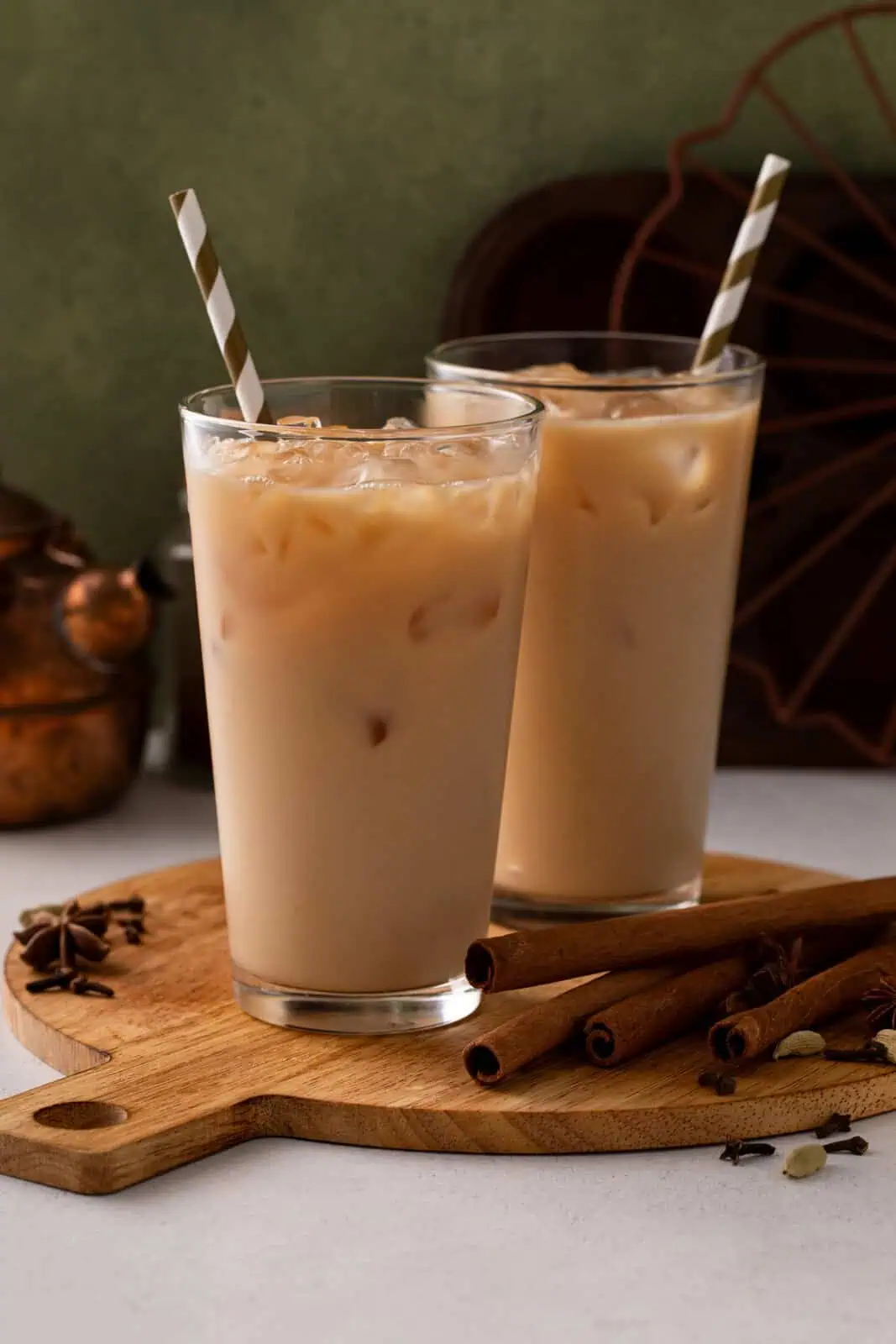 Two tall glasses filled with iced chai lattes, each with a striped paper straw in them.