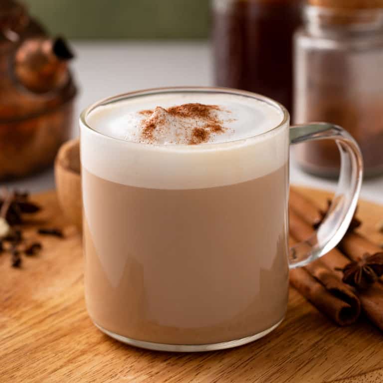 Hot chai latte in a glass mug set on a wooden board.