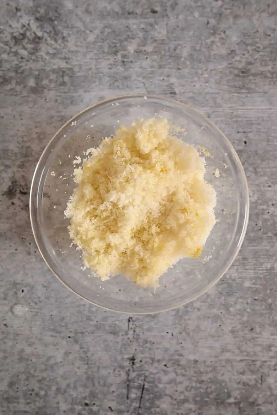 Lemon sugar in a small glass bowl set on a concrete countertop.