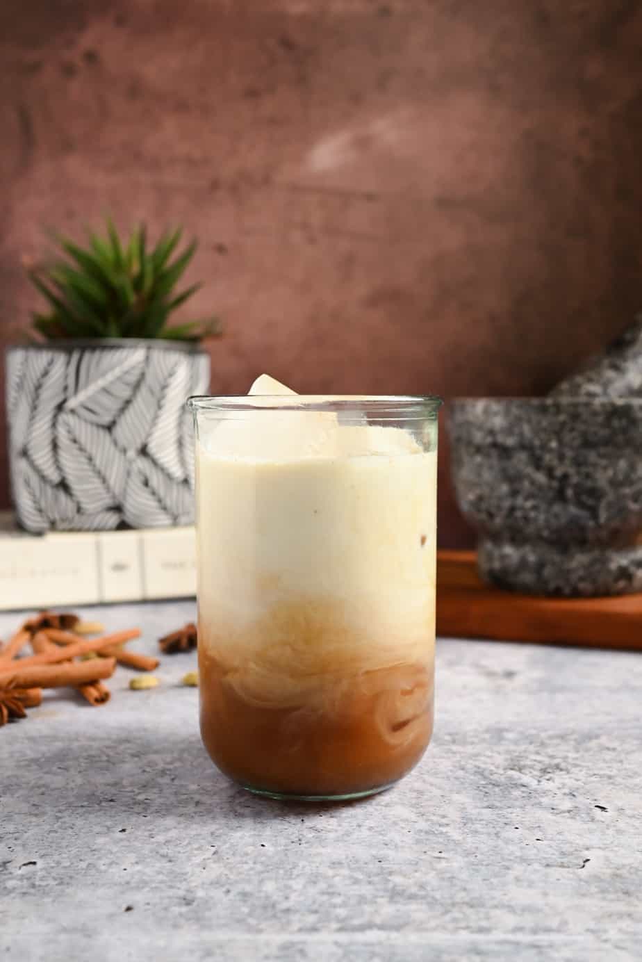Milk mixing with chai concentrate in a glass, set on a cement countertop