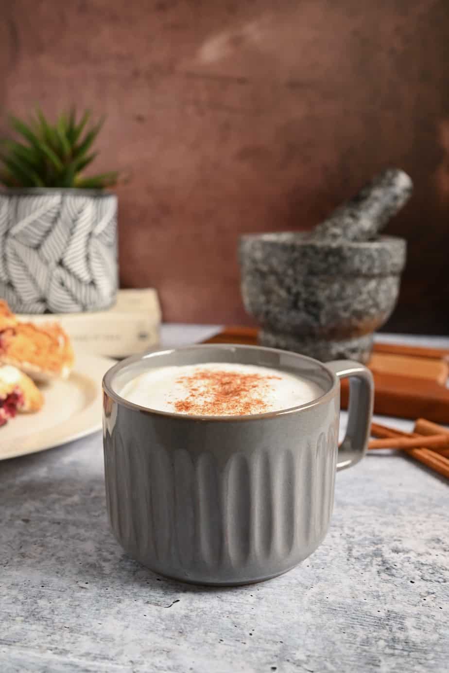 Gray mug filled with chai latte in front of a plate of scones