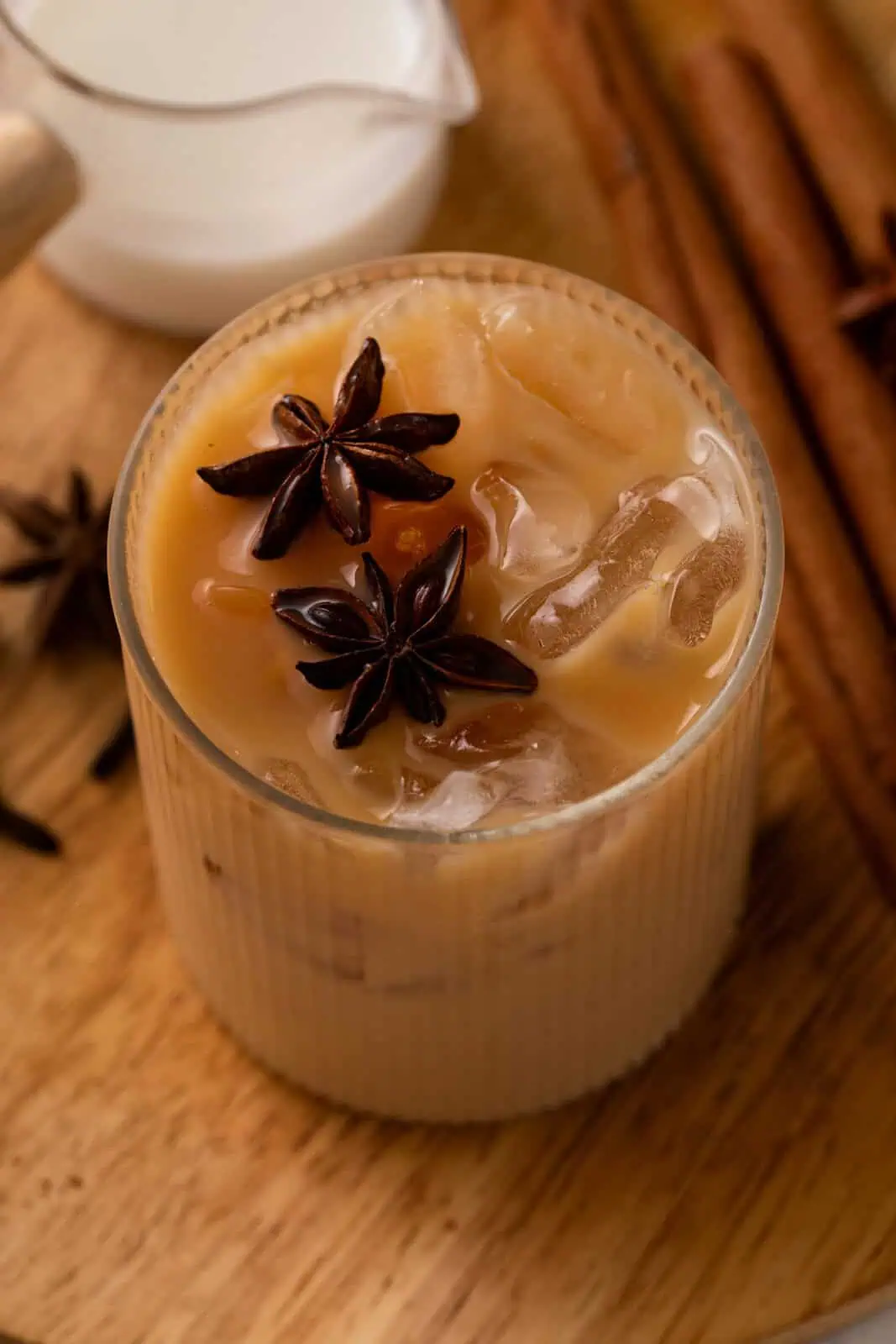 Overhead view of an iced chai latte in a glass, garnished with two star anise pods.