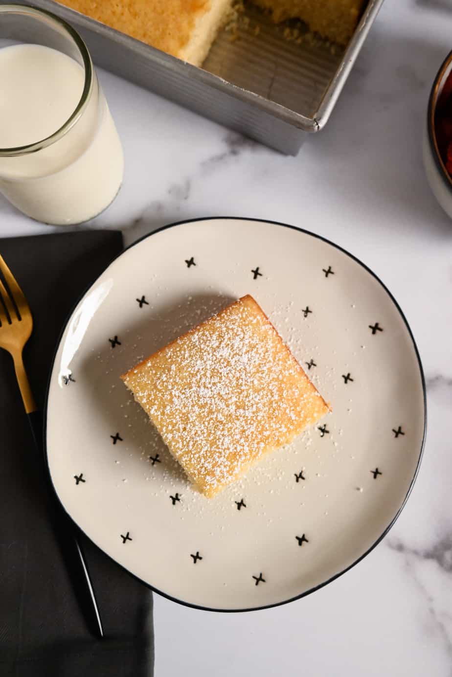 Slice of yellow cake dusted with powdered sugar on a white and black plate