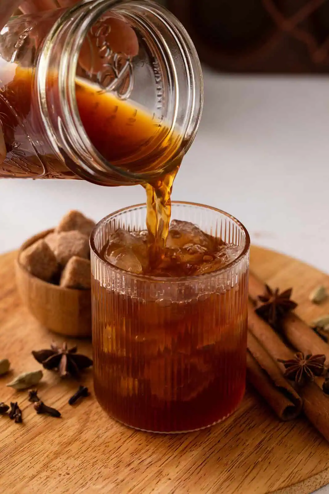 Homemade chai concentrate being poured over ice in a glass.