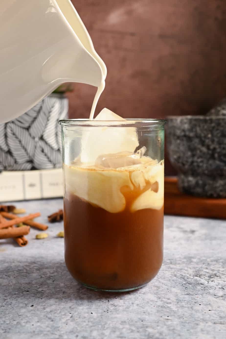 Milk being poured over chai concentrate and ice in a glass