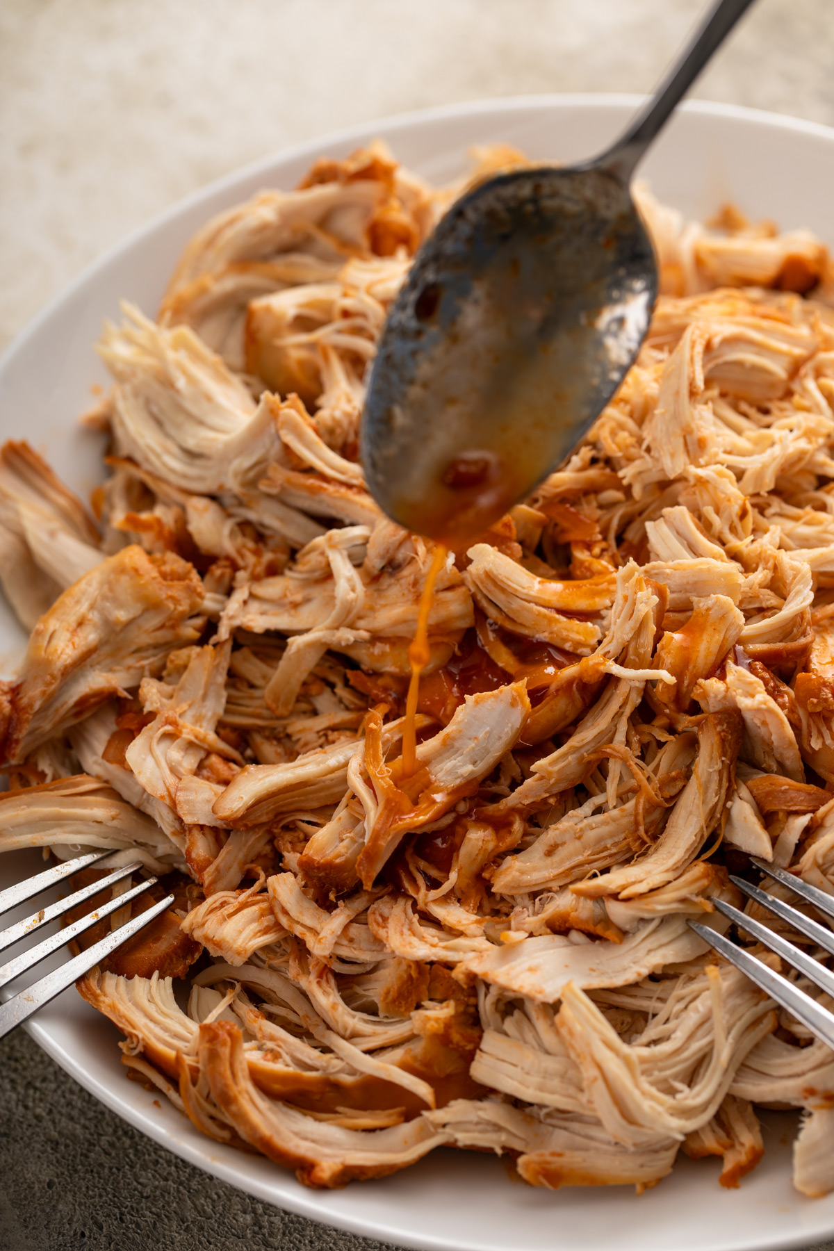 Spooning cooking juices over shredded chicken in a mixing bowl.