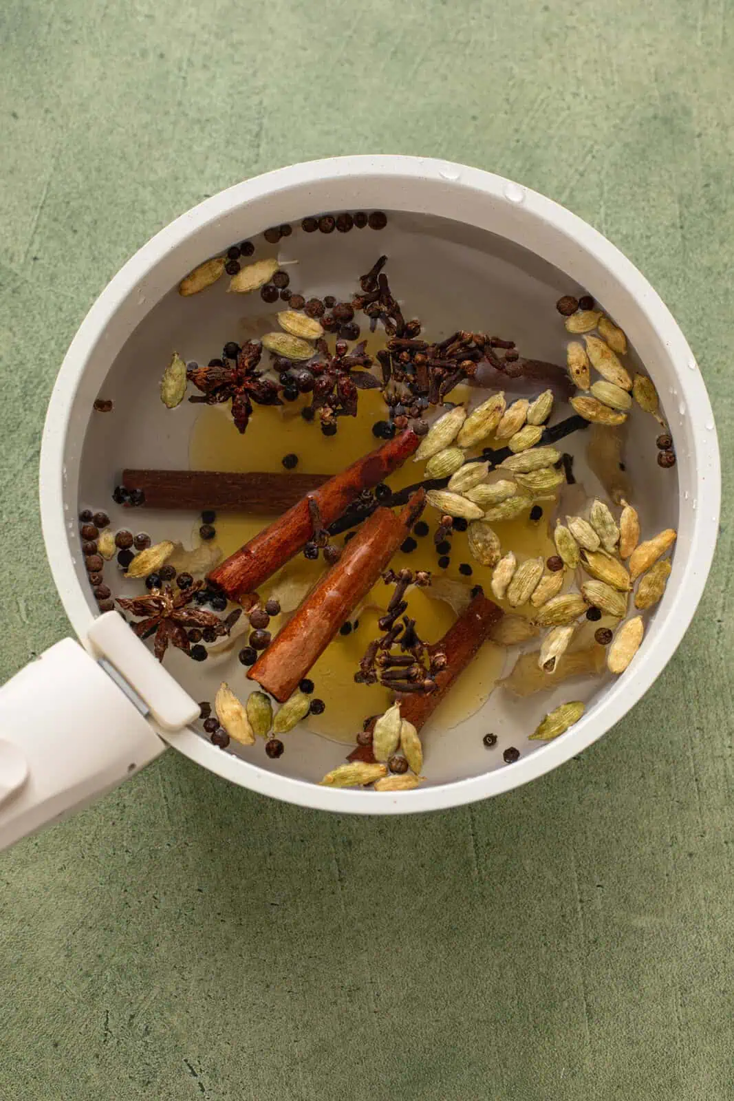 Whole spices, water, and honey in a white saucepan.