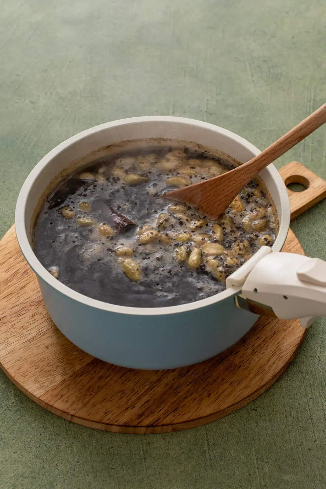 Wooden spoon stirring chai concentrate in a saucepot.