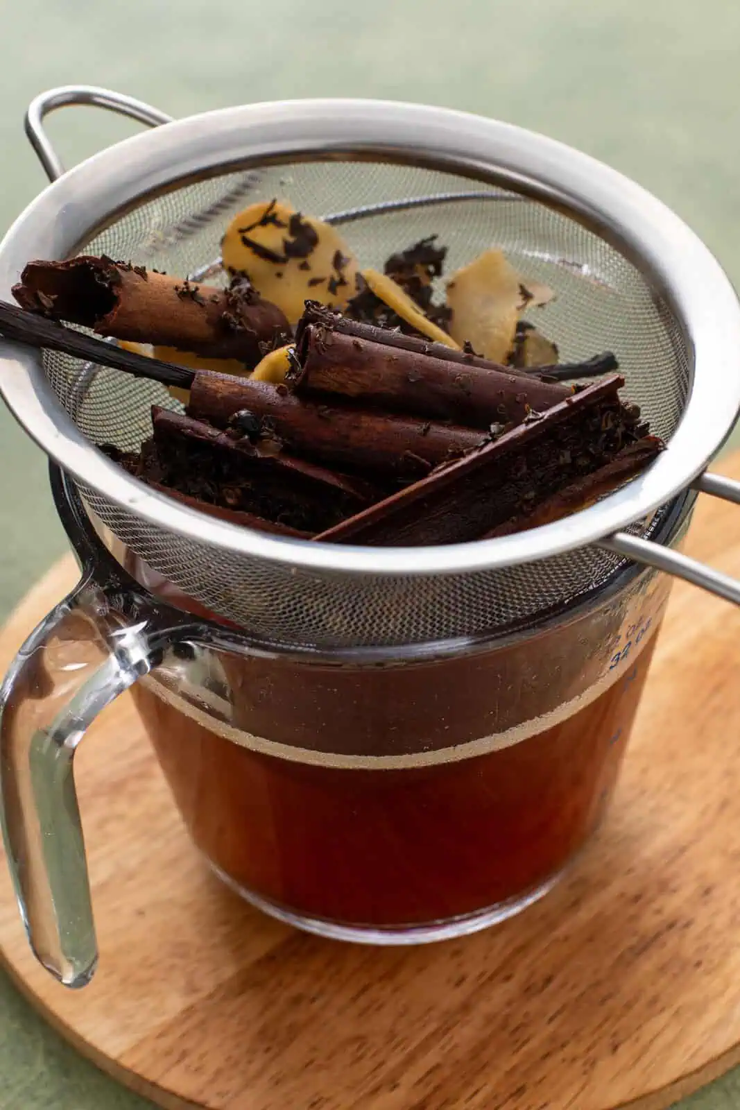 Chai concentrate strained through a mesh sieve, with the whole spices and tea leaves caught in the sieve.