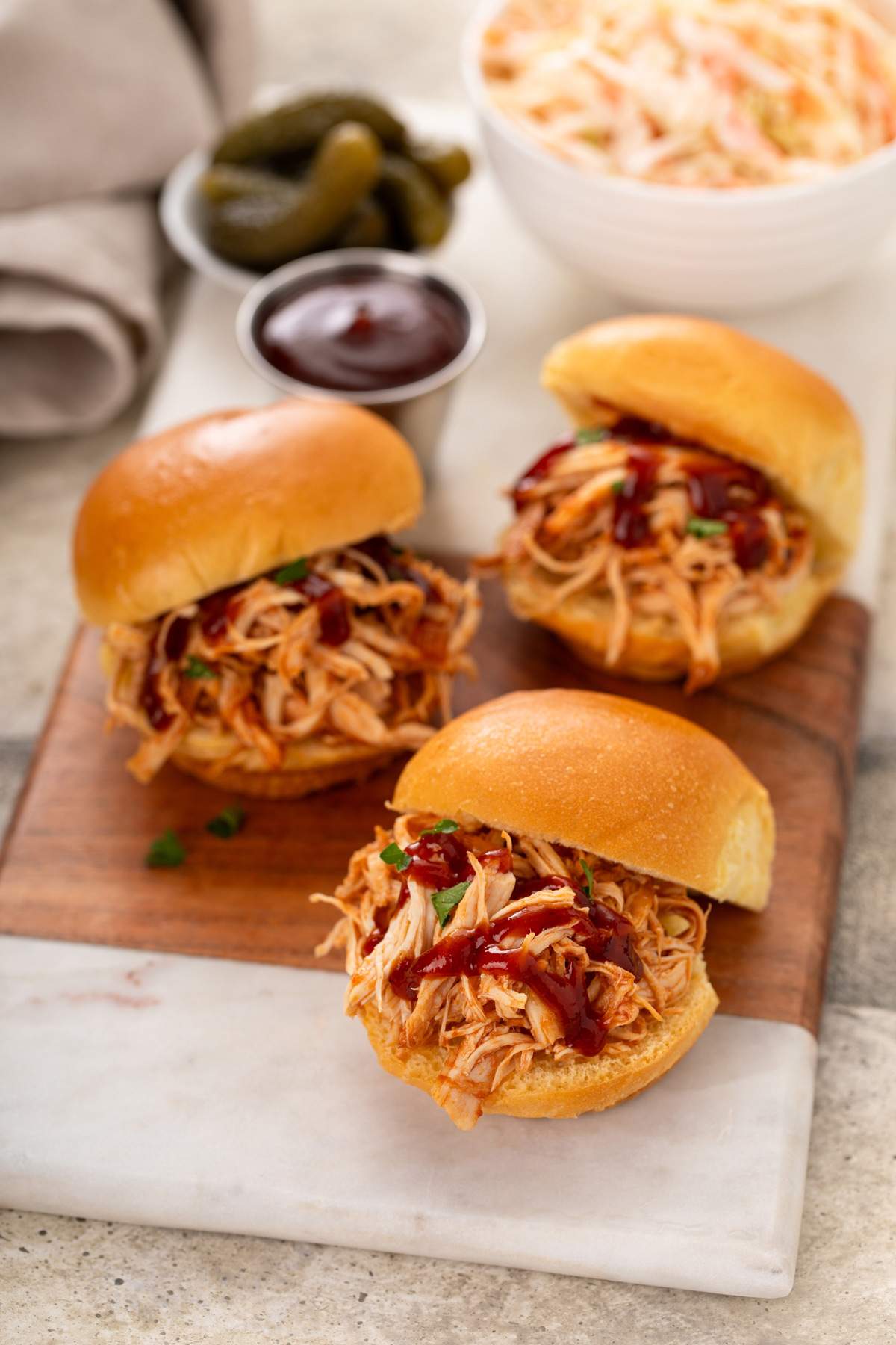 Three pulled chicken sliders topped with a drizzle of barbecue sauce arranged on a cutting board.