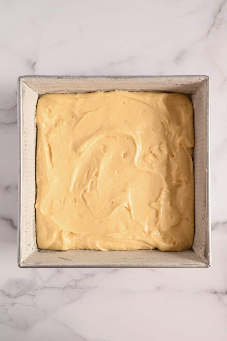 Yellow cake batter in a square cake pan, ready to go in the oven.