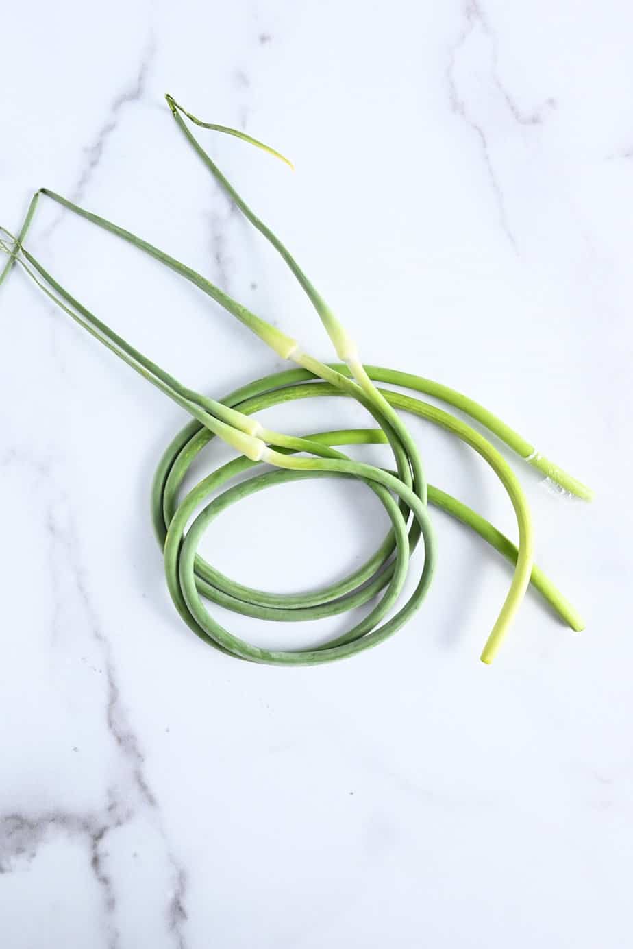 Bundle of fresh garlic scapes set on a marble countertop.