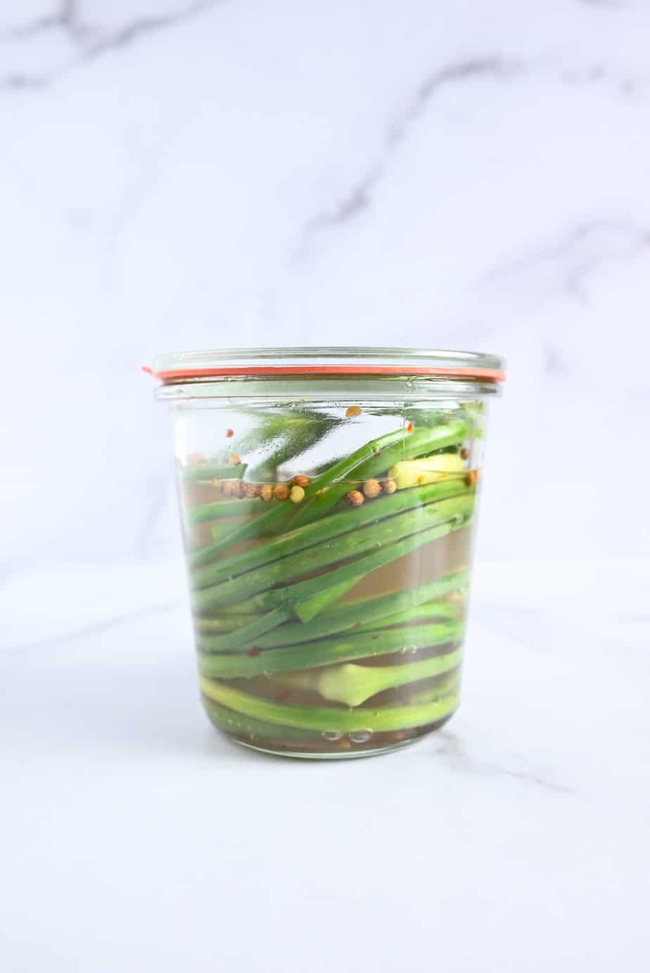 Fresh garlic scapes in a glass jar with brine poured over them.