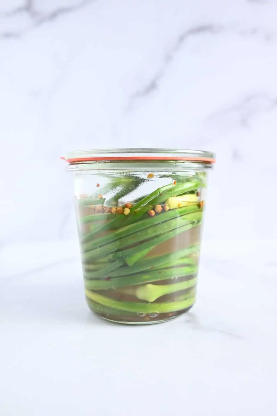 Fresh garlic scapes in a glass jar with brine poured over them.