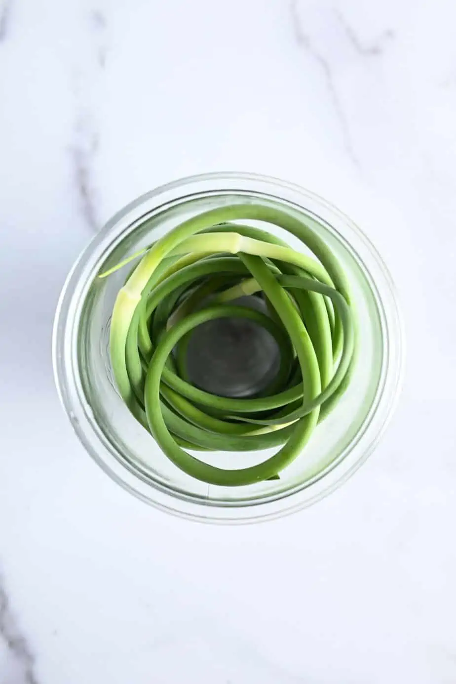 Fresh garlic scapes arranged in a glass jar.