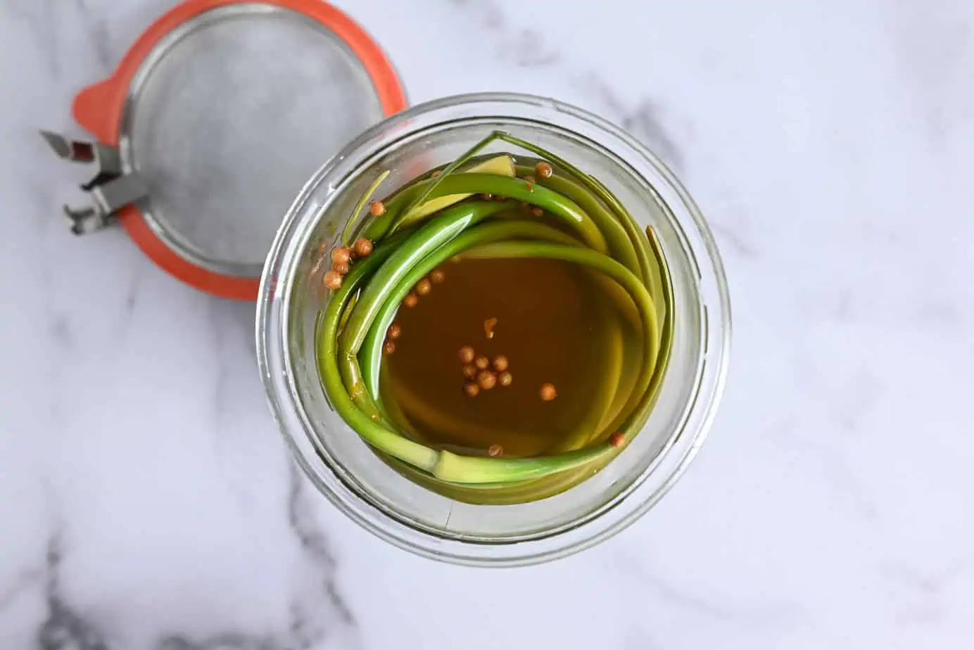 Close-up overhead view of pickled garlic scapes in a wide-mouth glass jar.