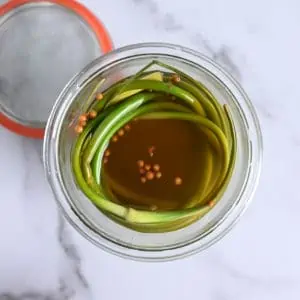 Close up view of pickled garlic scapes in an open glass jar.