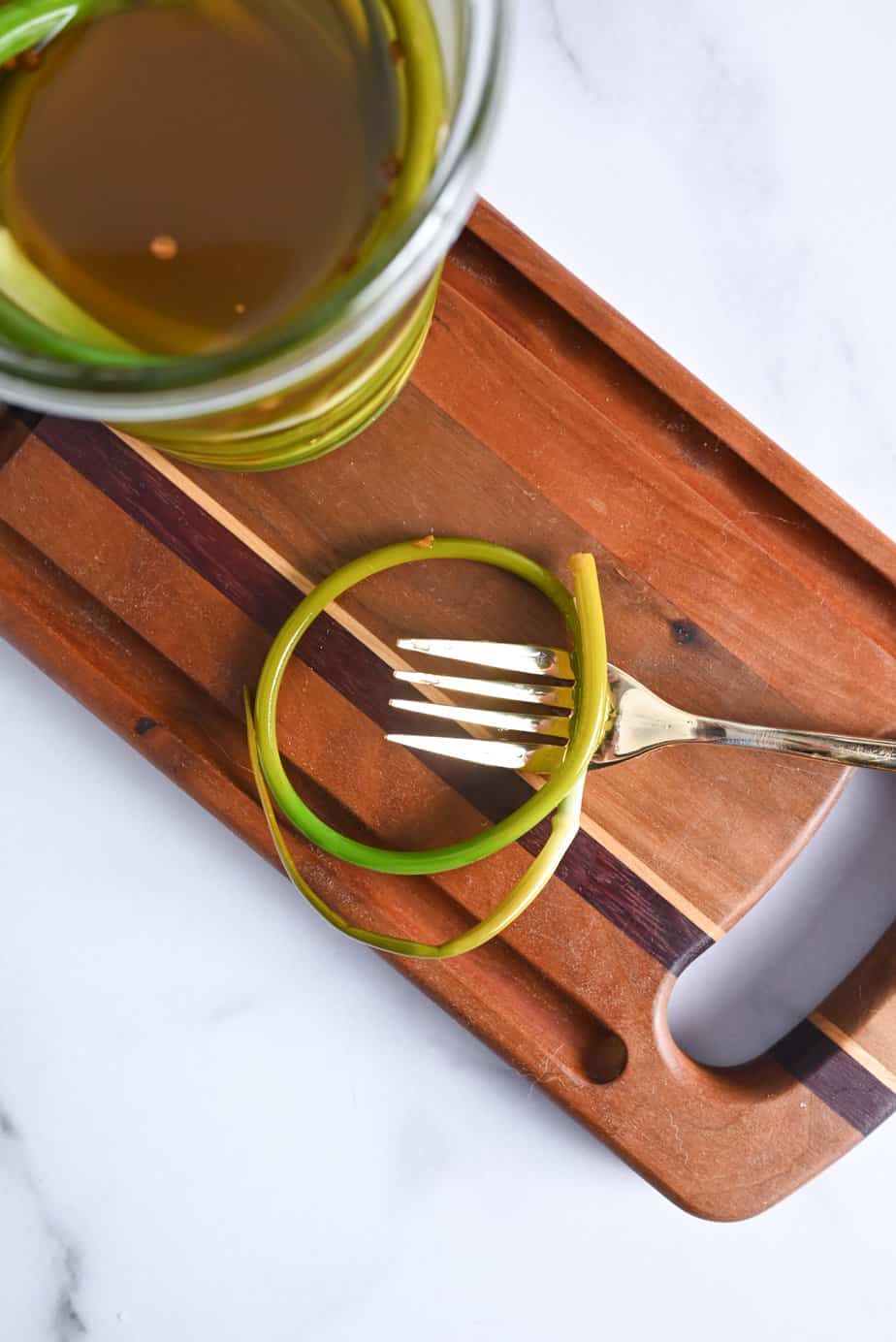 Pickled garlic scape on a fork set on a wooden cutting board.
