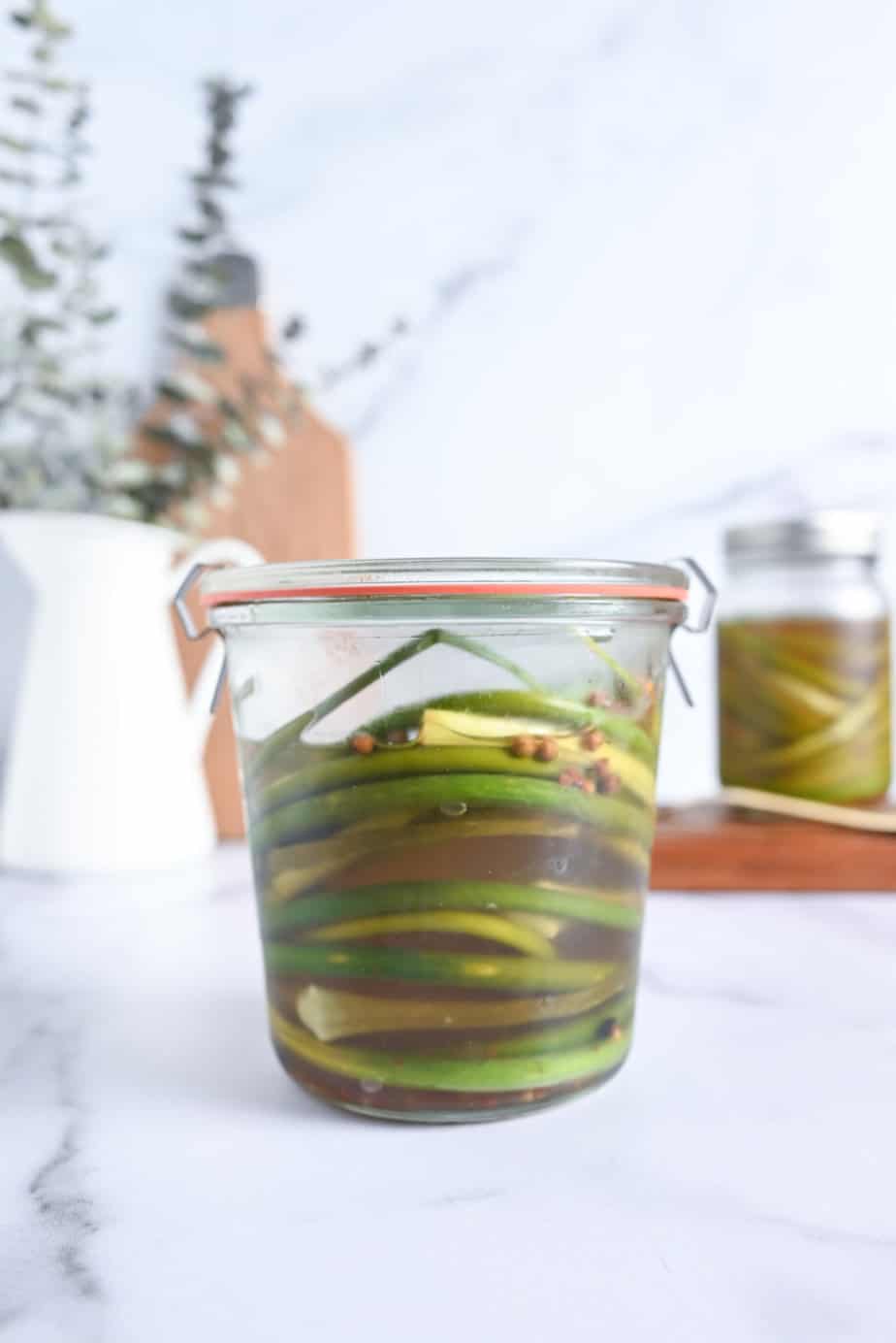 Closed jar of pickled garlic scapes set on a marble countertop.
