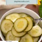 Fork lifting some slices of pickled cucumber out of a white bowl. Text overlay includes recipe name.