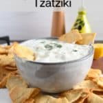 Gray bowl holding homemade tzatziki set on a platter next to pita chips. Text overlay includes recipe name.