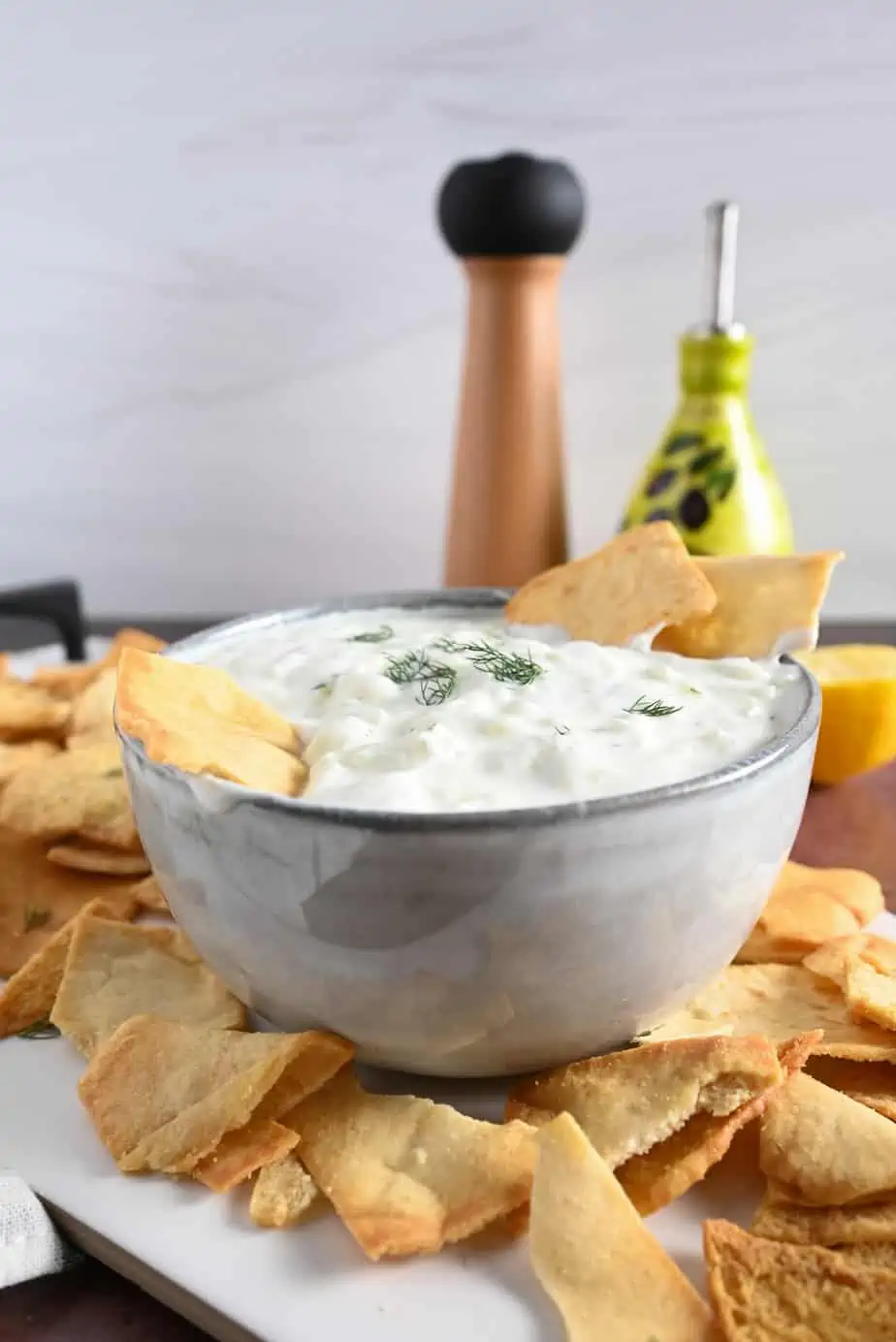 Gray bowl holding homemade tzatziki set on a platter next to pita chips.