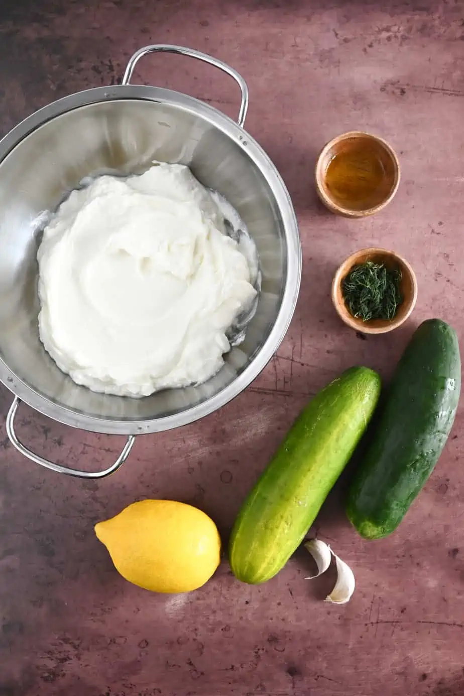 Ingredients for homemade tzatziki arranged on a dark countertop.