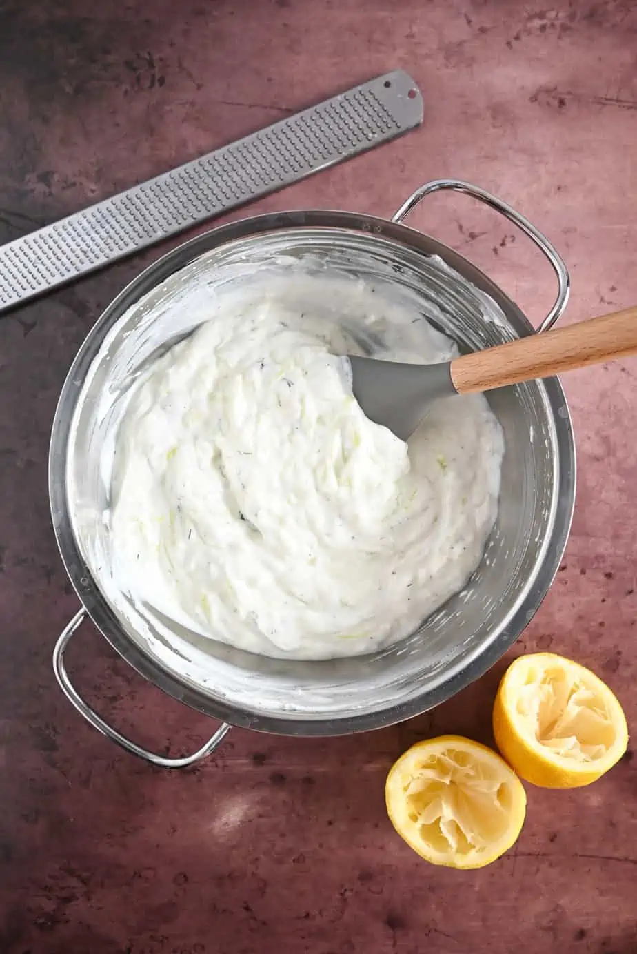 Homemade tzatziki being stirred with a spatula in a metal mixing bowl.