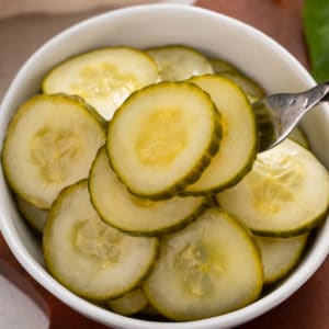 Fork lifting up pickled cucumbers from a bowl.