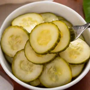 Fork lifting up pickled cucumbers from a bowl.