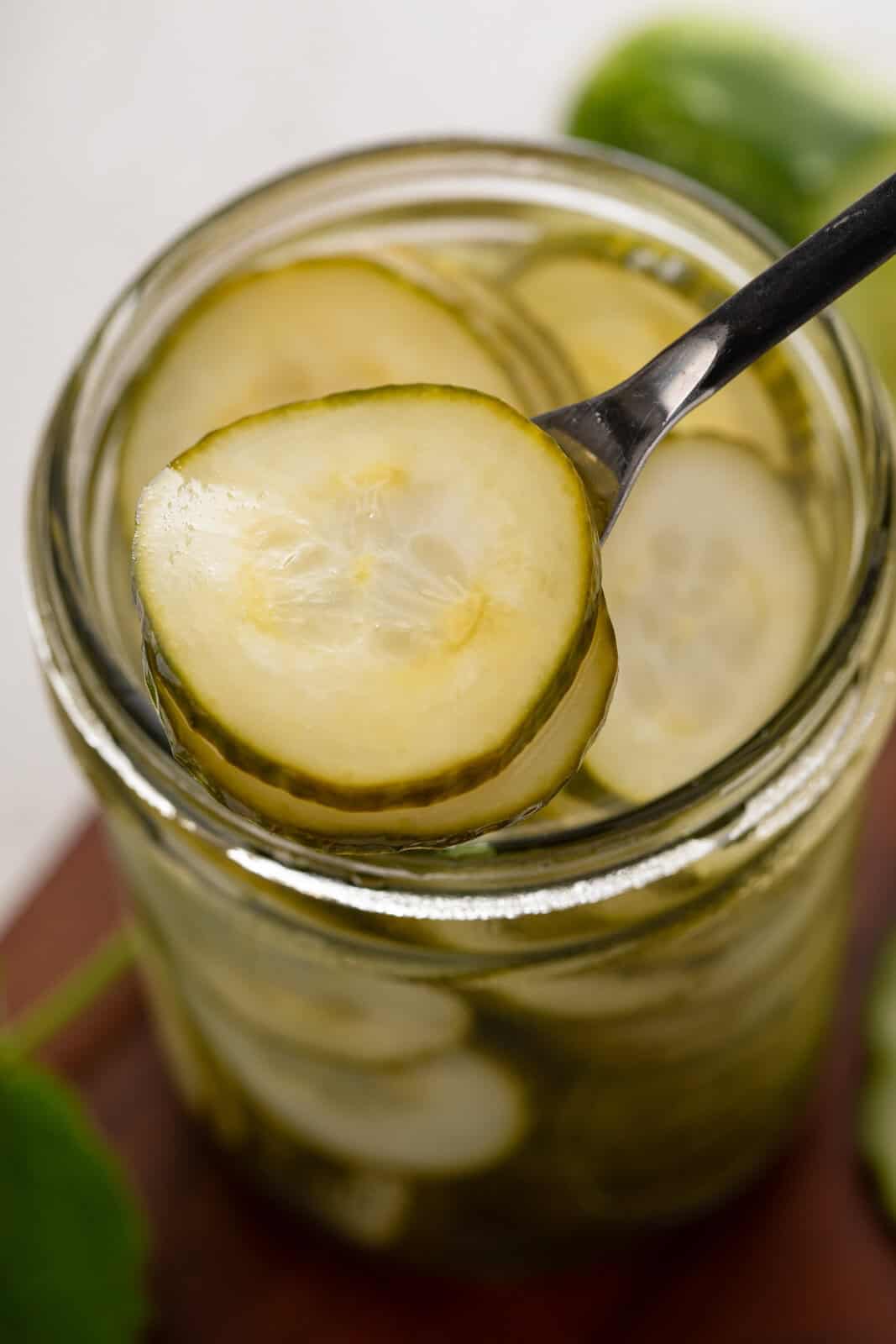 Fork lifting slices of pickled cucumbers from a glass jar.