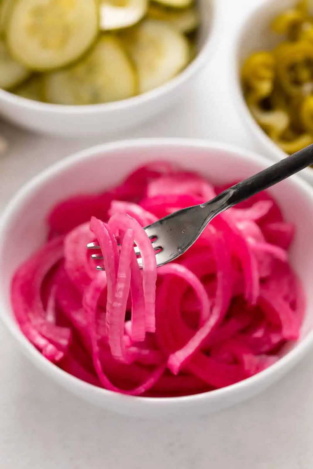 Fork picking up slices of pickled red onion from a white bowl.