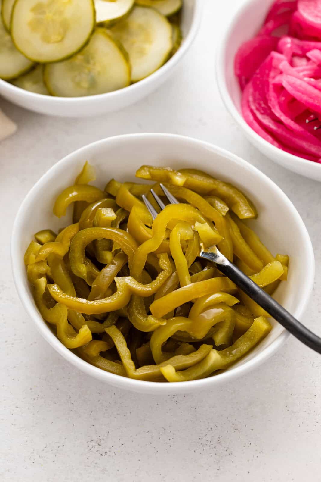 Fork set in a white bowl of pickled green pepper slices.