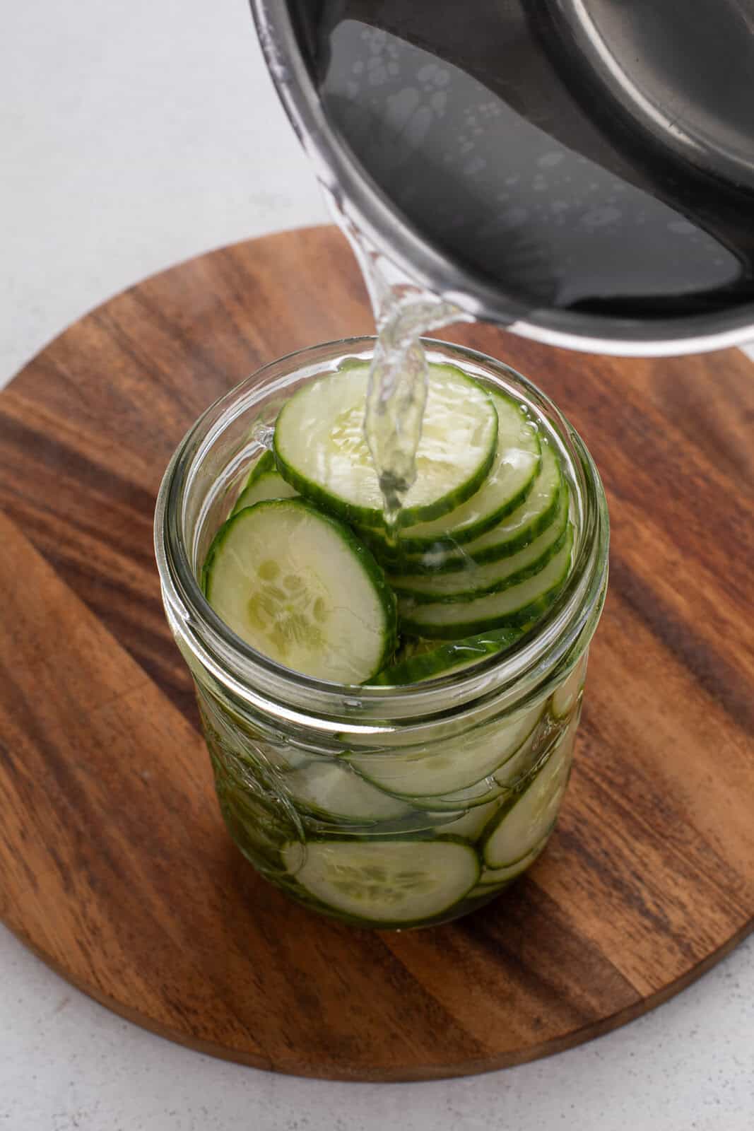 Brine being poured over sliced cucumbers in a jar.