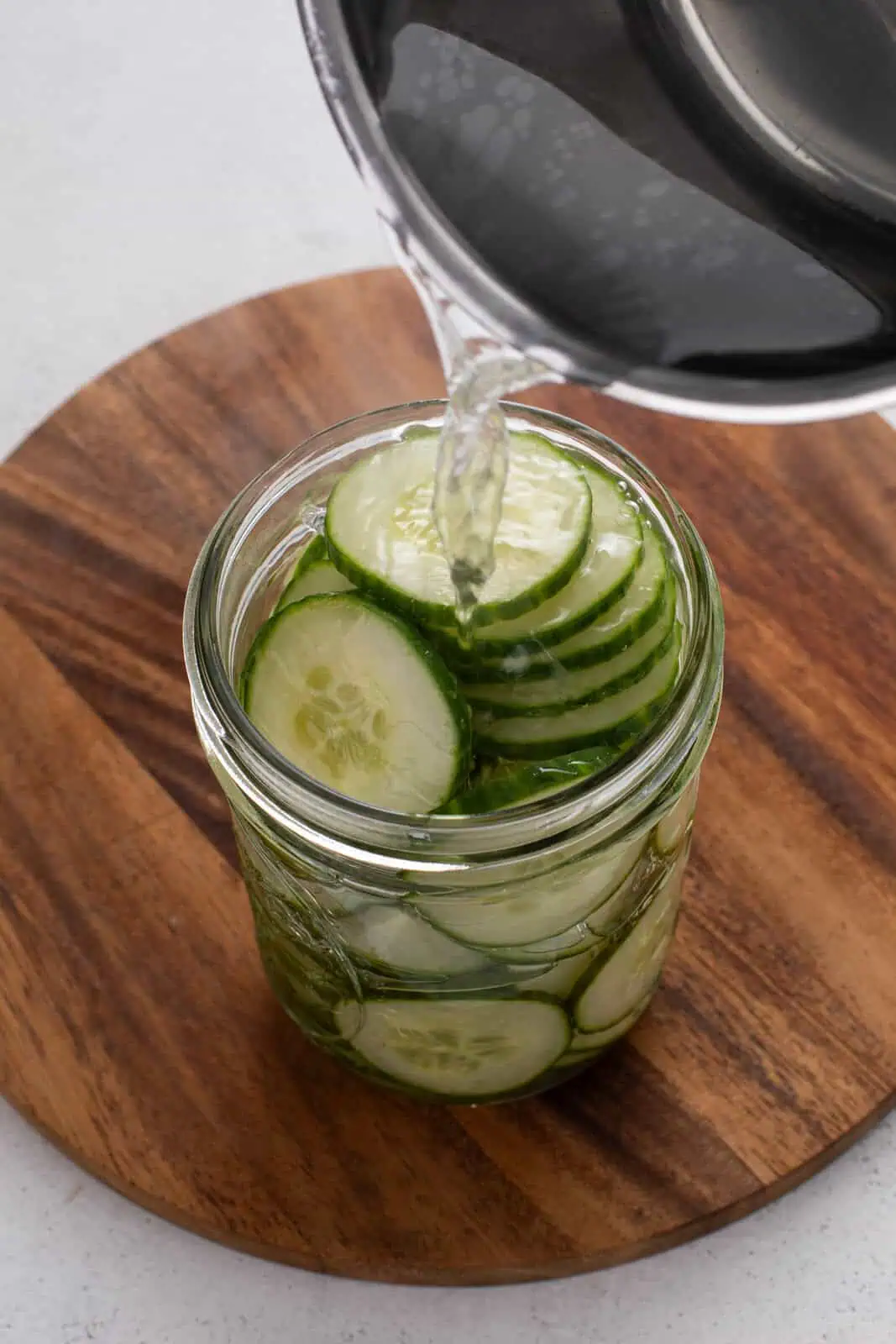 Brine being poured over sliced cucumbers in a jar.