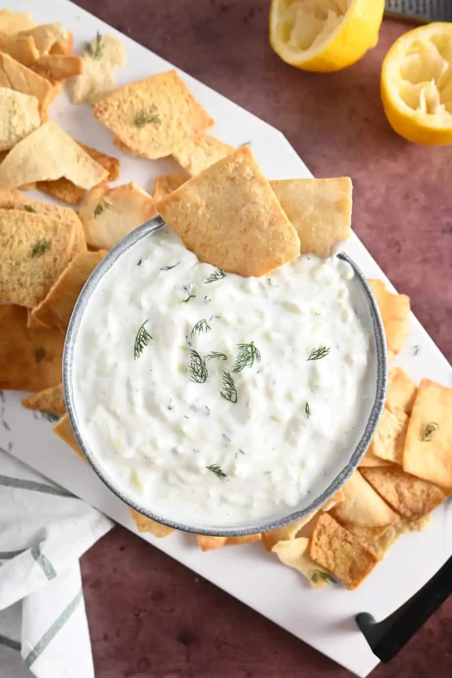 Two pita chips along the edge of a bowl of homemade tzatziki. The bowl is surrounded by pita chips.