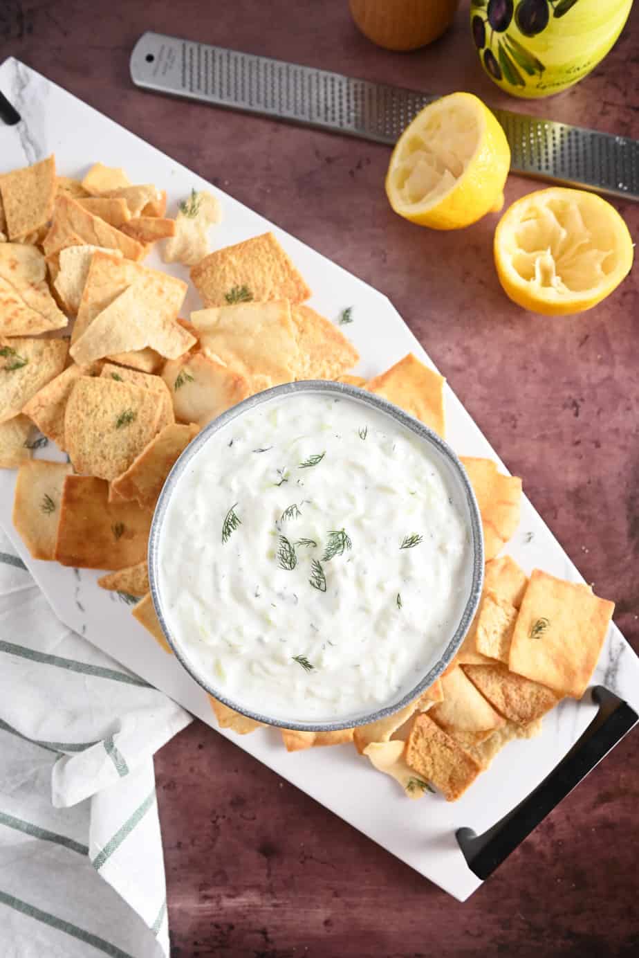 Overhead view of a Bowl of homemade tzatziki on a marble platter, surrounded by pita chips.