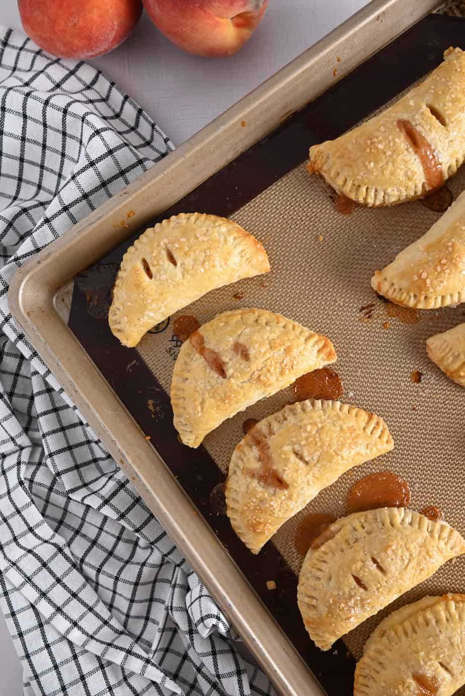 Baked peach hand pies on a baking sheet lined with a silicone mat.
