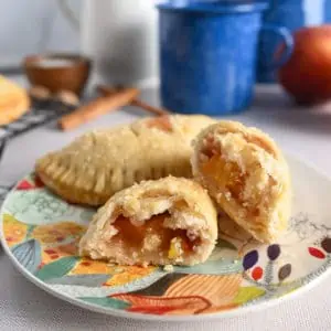 Two peach hand pies, one of them cut in half, on a brightly colored flowered plate.