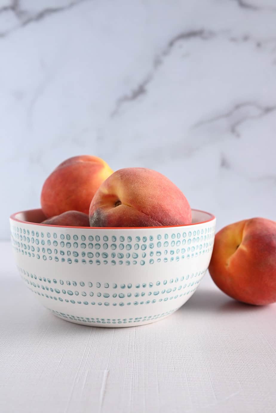 Fresh peaches in a blue and white bowl set on a tabletop.