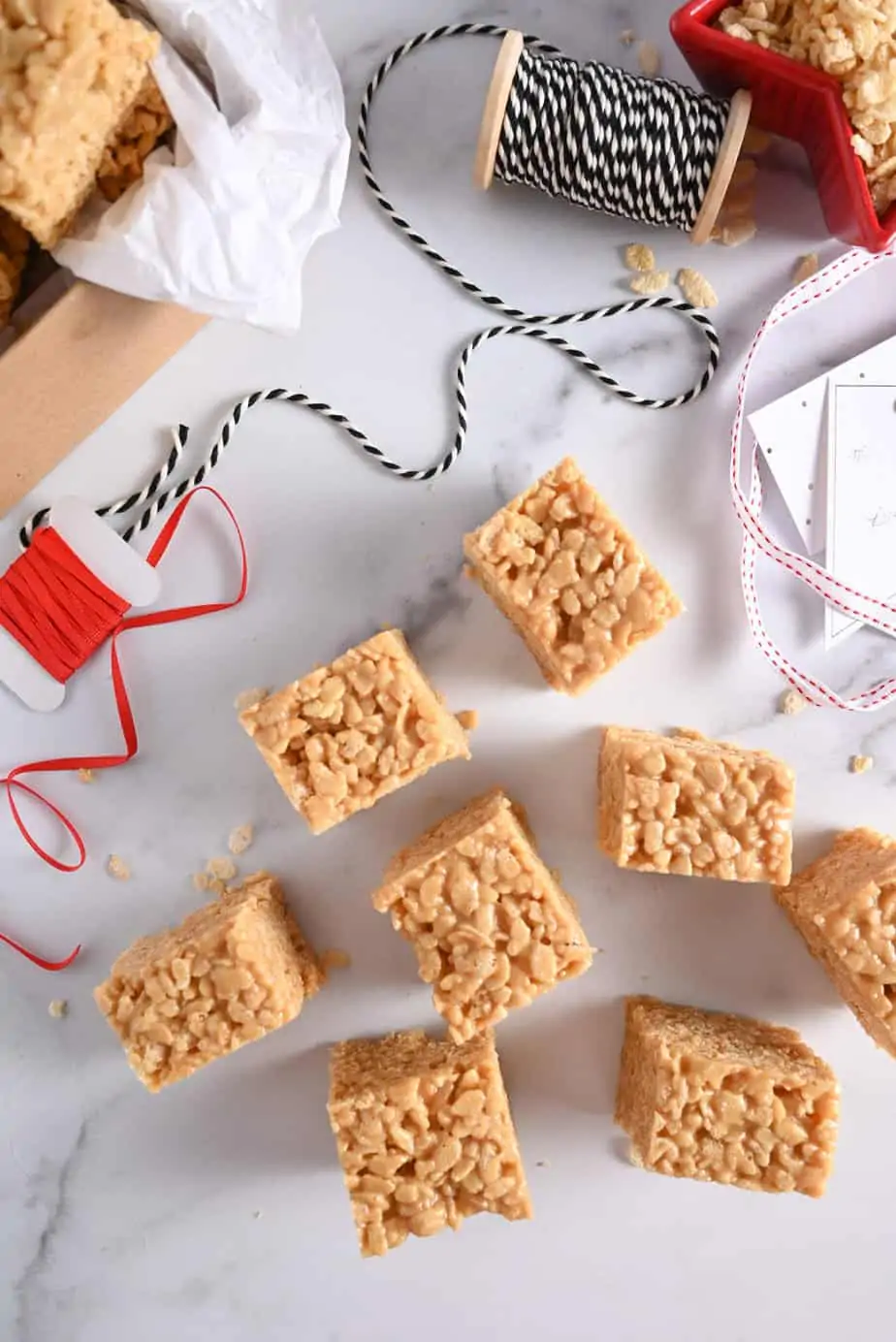 Several peanut butter rice krispie bars scattered on a marble countertop, about to be packaged up for the holidays.