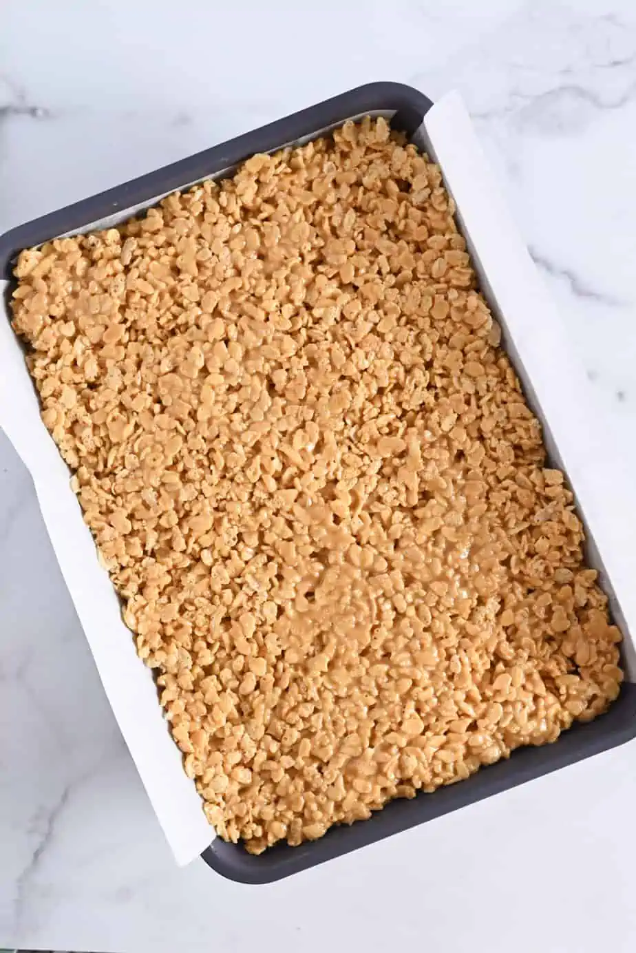 Peanut butter rice krispie bars pressed into a parchment-lined baking pan.