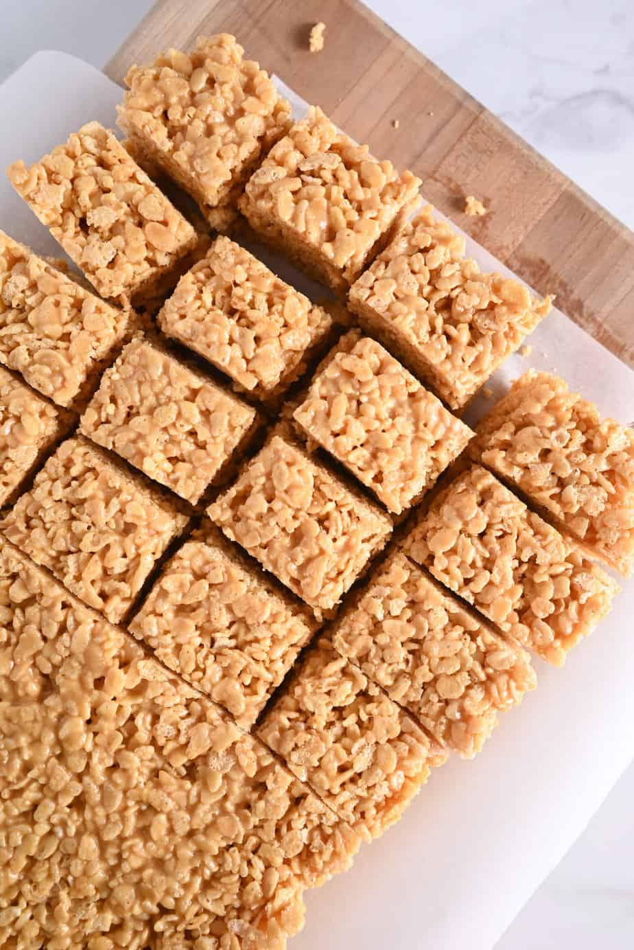 Slab of peanut butter rice krispie bars being sliced on a wooden cutting board.