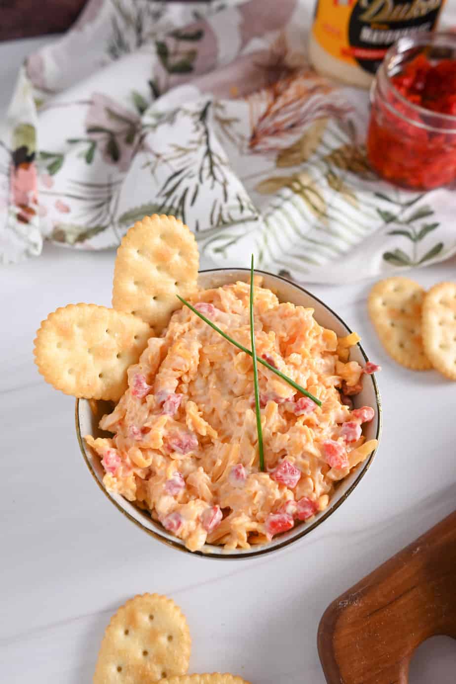 Overhead view of a white bowl filled with pimento cheese and garnished with chives and crackers.