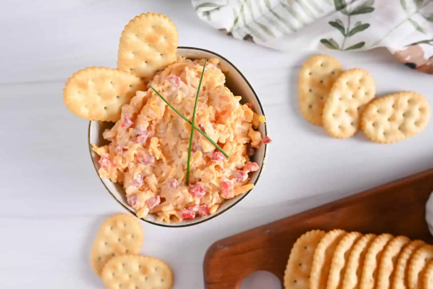 Bowl of pimento cheese next to a cutting board with crackers on it.