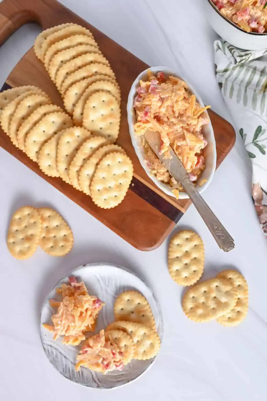 White plate filled with crackers and pimento cheese next to a cutting board holding a dish of pimento cheese and crackers.