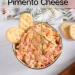Overhead view of a white bowl filled with pimento cheese and garnished with chives and crackers. Text overlay includes recipe name.