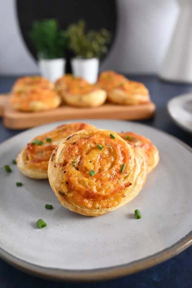 Three hot ham and cheese pinwheels on a gray plate with a platter of more pinwheels in the background.