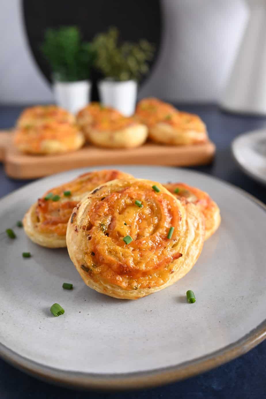 Three hot ham and cheese pinwheels on a gray plate with a platter of more pinwheels in the background.