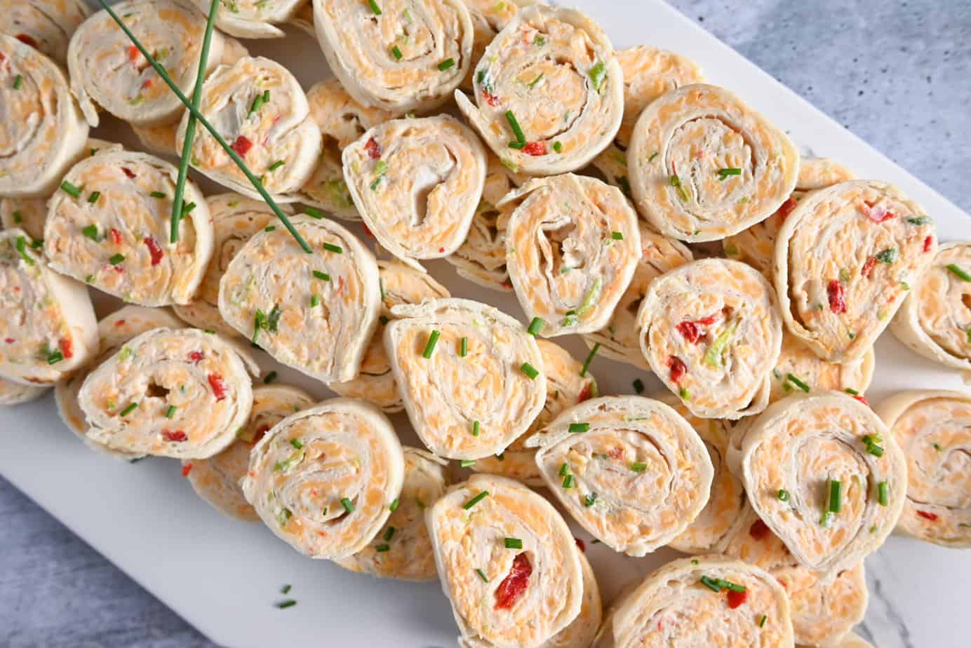 Close up of a white platter filled with pimento cheese pinwheels and garnished with chives.